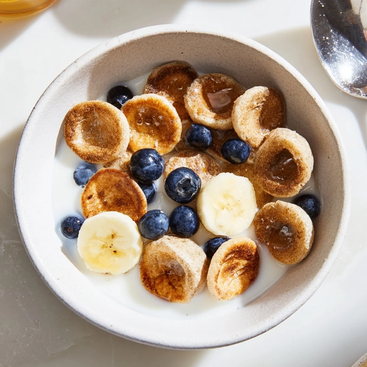 Cheerful bite-sized pancake cereal drizzled with honey and accompanied by bananas.