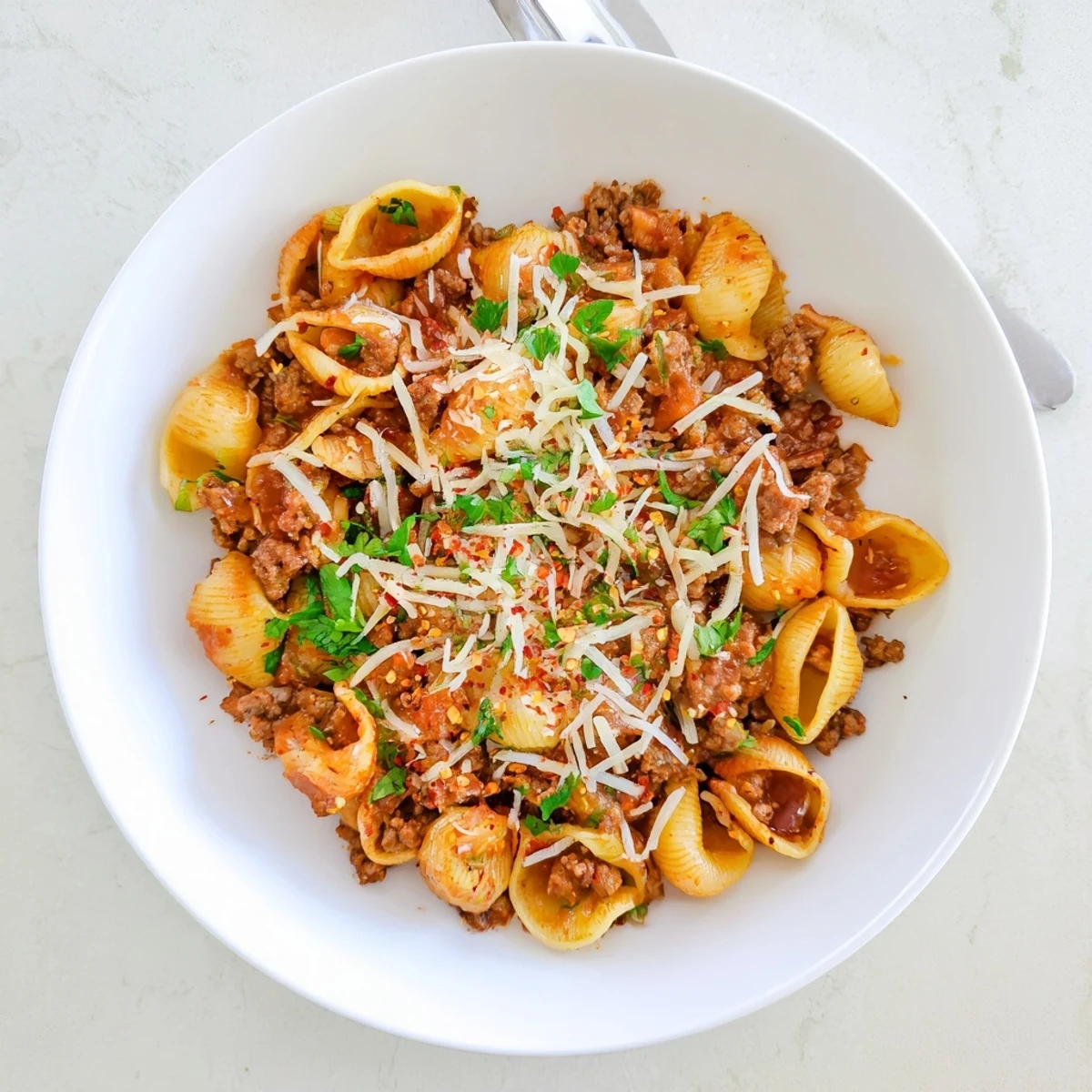 A steaming bowl of One Pot Creamy Beef and Shells pasta, featuring tender ground beef nestled inside shell pasta coated in a rich, cheesy tomato sauce.
