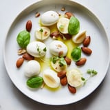 A beautiful spread of The Polished Pebble, featuring oval cheeses and roasted almonds, drizzled in olive oil.