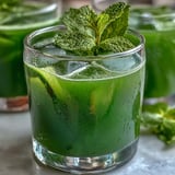 A vibrant glass of cucumber, apple, and ginger detox juice with fresh mint garnish.  