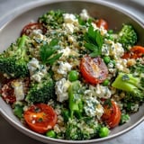 Nutty quinoa mixed with tender broccoli, green peas, and juicy cherry tomatoes, topped with creamy feta and parsley for a protein-packed lunch.