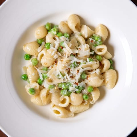 A close-up of delicious macaroni & peas, showing the creamy sauce and tender green peas.