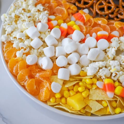 An inviting candy corn spooky board features marshmallows, cheese, and vibrant fruit for a treat.