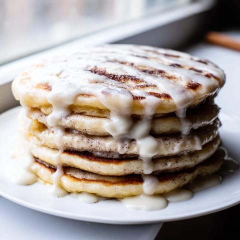 Warm, fluffy cinnamon roll pancakes, drizzled with sweet cream cheese frosting, ready to eat.