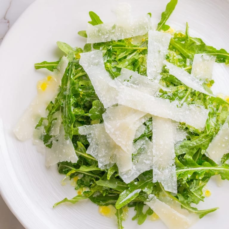 Vibrant plate of arugula salad, its lemon dressing clinging to leaves, finished with Parmesan.