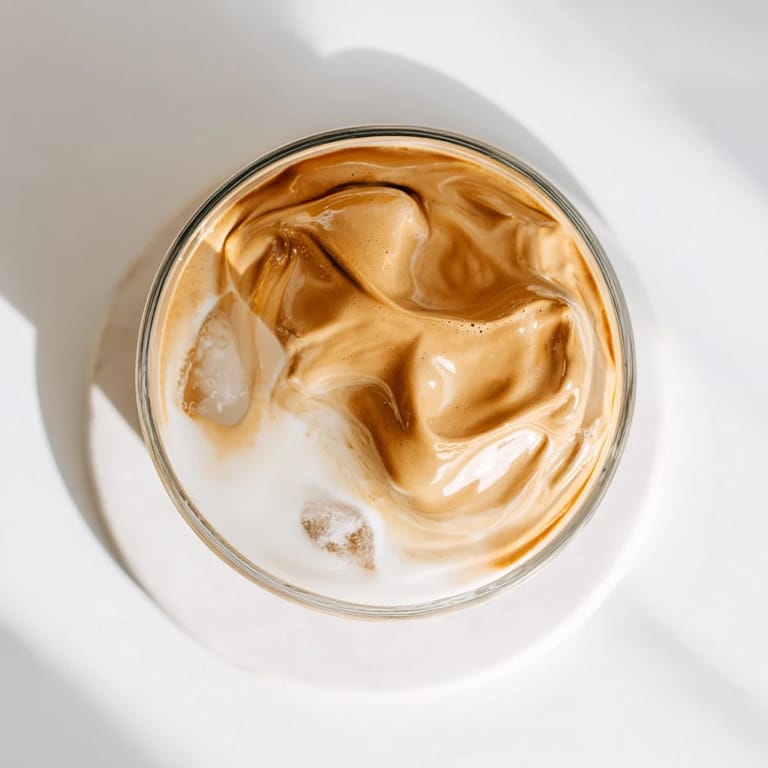 Homemade Whipped Dalgona Coffee in a clear glass, showcasing fluffy whipped coffee over dairy or plant-based milk.